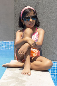 Full length of girl wearing sunglasses sitting on swimming pool