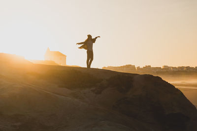 Man standing on rock against sky during sunset