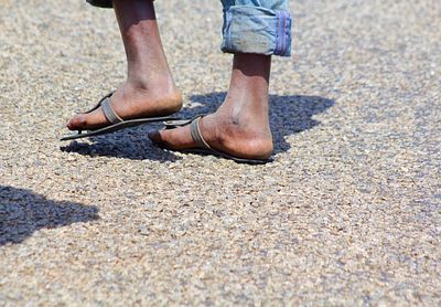 Low section of man walking on road during sunny day