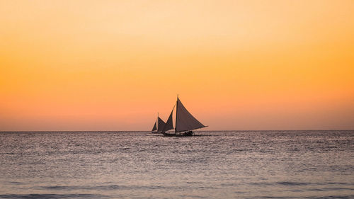 Sailboat sailing on sea against orange sky