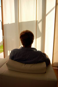 Rear view of man looking through window at home