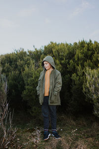 Boy standing by tree against sky