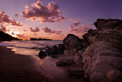 Rocks on beach against sky during sunset