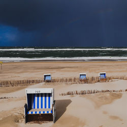 Hooded beach chairs on shore against sky