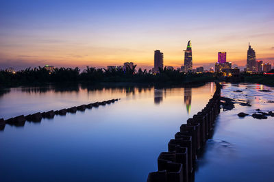 Scenic view of river by buildings against sky during sunset