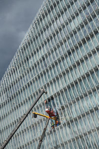 Low angle view of crane on building against sky