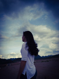 Young woman standing on land against sky during sunset