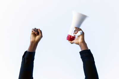 Unrecognizable crop african american male with red and white megaphone standing with fist up on white background