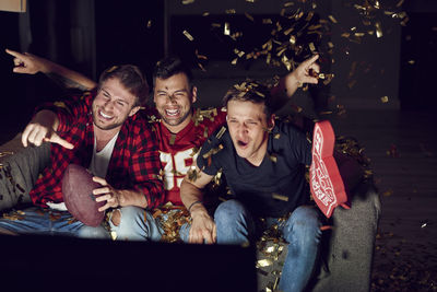 Friends cheering while looking at television set in living room