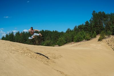 Man in mid-air performing stunt over sand against blue sky