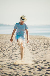 Full length of man kicking sand at beach