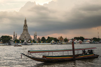 Boats in river by buildings against sky in city