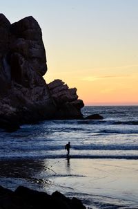 Silhouette man standing on rock by sea against sky