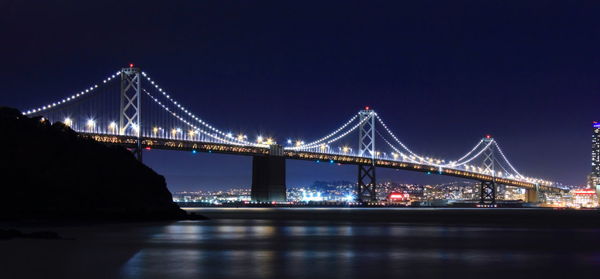 Illuminated san francisco–oakland bay bridge over sea against sky at night