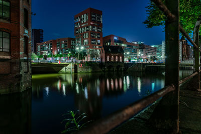 Illuminated buildings by river against sky at night