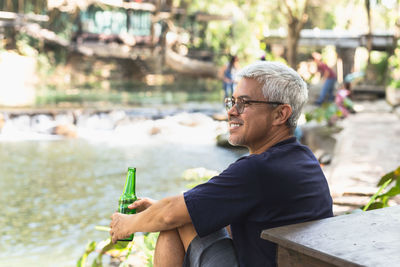 Happy man with smile hand holding bottel of beer with nuture outdoor.