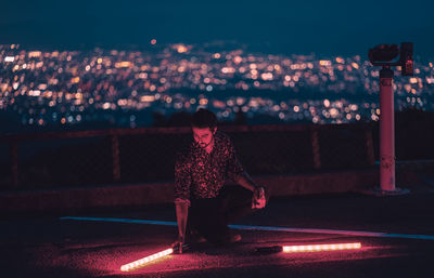 Full length of woman sitting on illuminated street at night