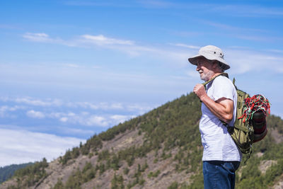 Side view of man wearing hat standing against sky