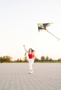 Full length portrait of woman with arms raised against clear sky