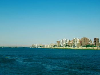 Scenic view of sea and buildings against clear blue sky