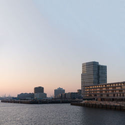 Sea by cityscape against clear sky during sunset