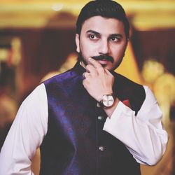 Young man touching mustache while standing indoors