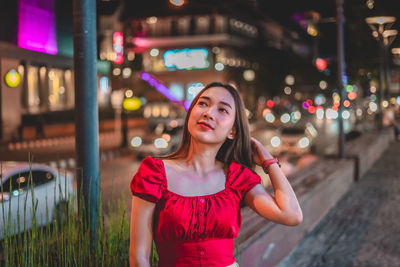 Young woman standing on footpath in city at night