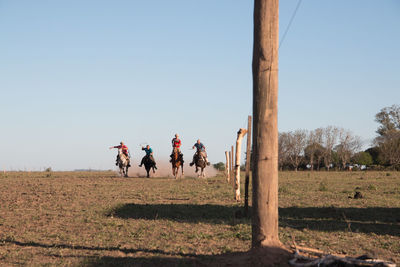 People on field riding horses against clear sky