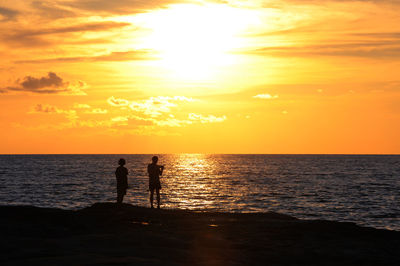 Silhouette people standing on sea against sky during sunset