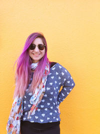 Portrait of smiling young woman standing against yellow wall