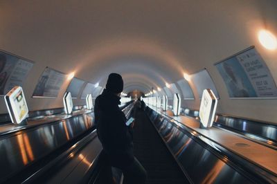 Rear view of man and woman standing on illuminated escalator
