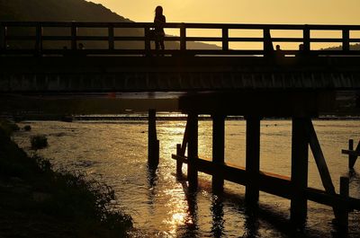 Silhouette man on footbridge over river against sky