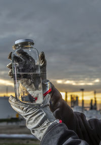 Close-up of hand holding glass against sky