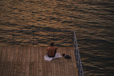Rear view of man sitting by sea on pier