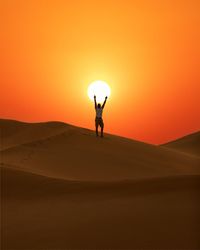 Man standing on sand dune against sky during sunset