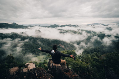 Rear view of man sitting against mountains during foggy weather