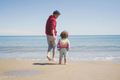 Rear view of boy standing at beach against clear sky