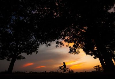 Silhouette people riding bicycle on field against sky during sunset