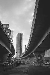 Bridge over city street by modern buildings against cloudy sky