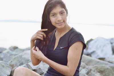 Portrait of smiling young woman standing at beach against sky