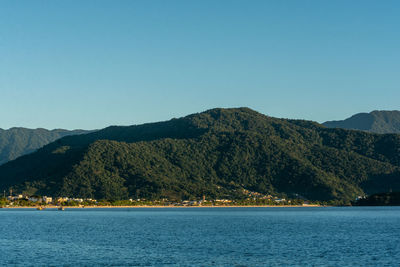 Scenic view of sea and mountains against clear blue sky