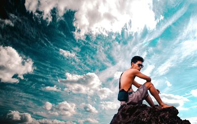 Man sitting on rock by sea against sky