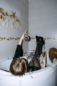 New years party celebration. happy young woman in evening dress sitting in the bathtub drinking