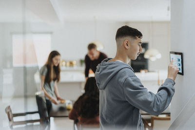 Teenage boy using digital tablet mounted on wall by family at modern home