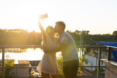 Rear view of couple standing on mobile phone against sky