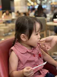 Cropped hand of parent feeding daughter sitting on chair in restaurant