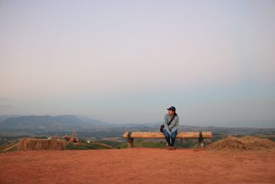 Full length of woman sitting on bench against sky during sunset