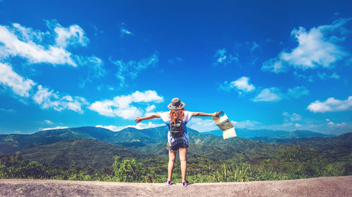 Rear view of woman with arms outstretched standing on mountain against sky