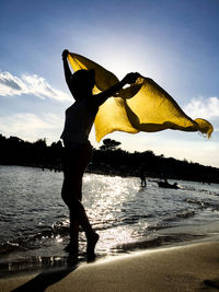 Woman holding textile while standing at beach against sky 