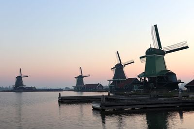 Traditional windmill by lake against clear sky during sunset